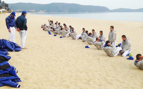 모래사장에 유니폼을 입은 선수들이 서로 짝을지어 윗몸일으키키 운동을 하고 있는 모습